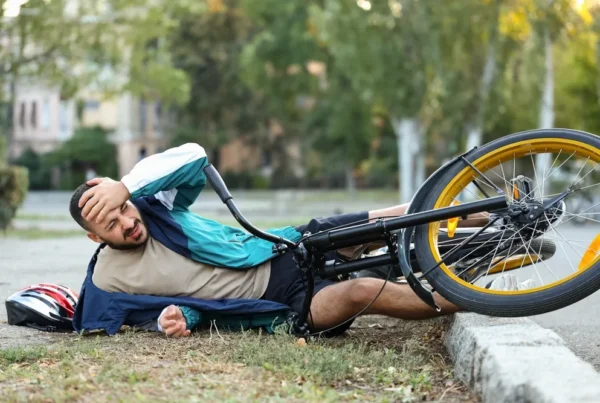 A man lies on the ground beside his bicycle, appearing relaxed in an outdoor setting.