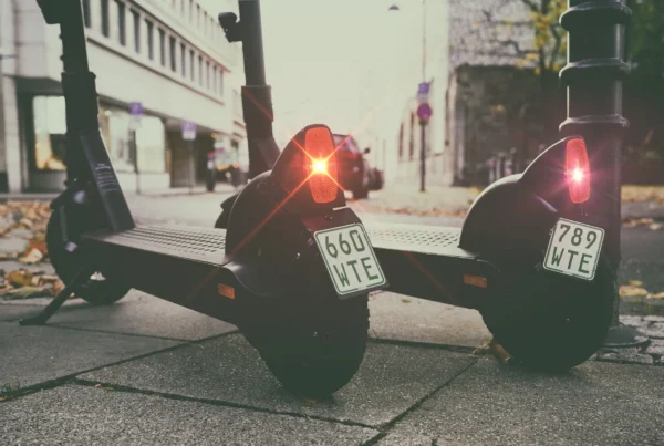 Two electric scooters parked side by side on a sidewalk, with a clear view of the surrounding urban environment.